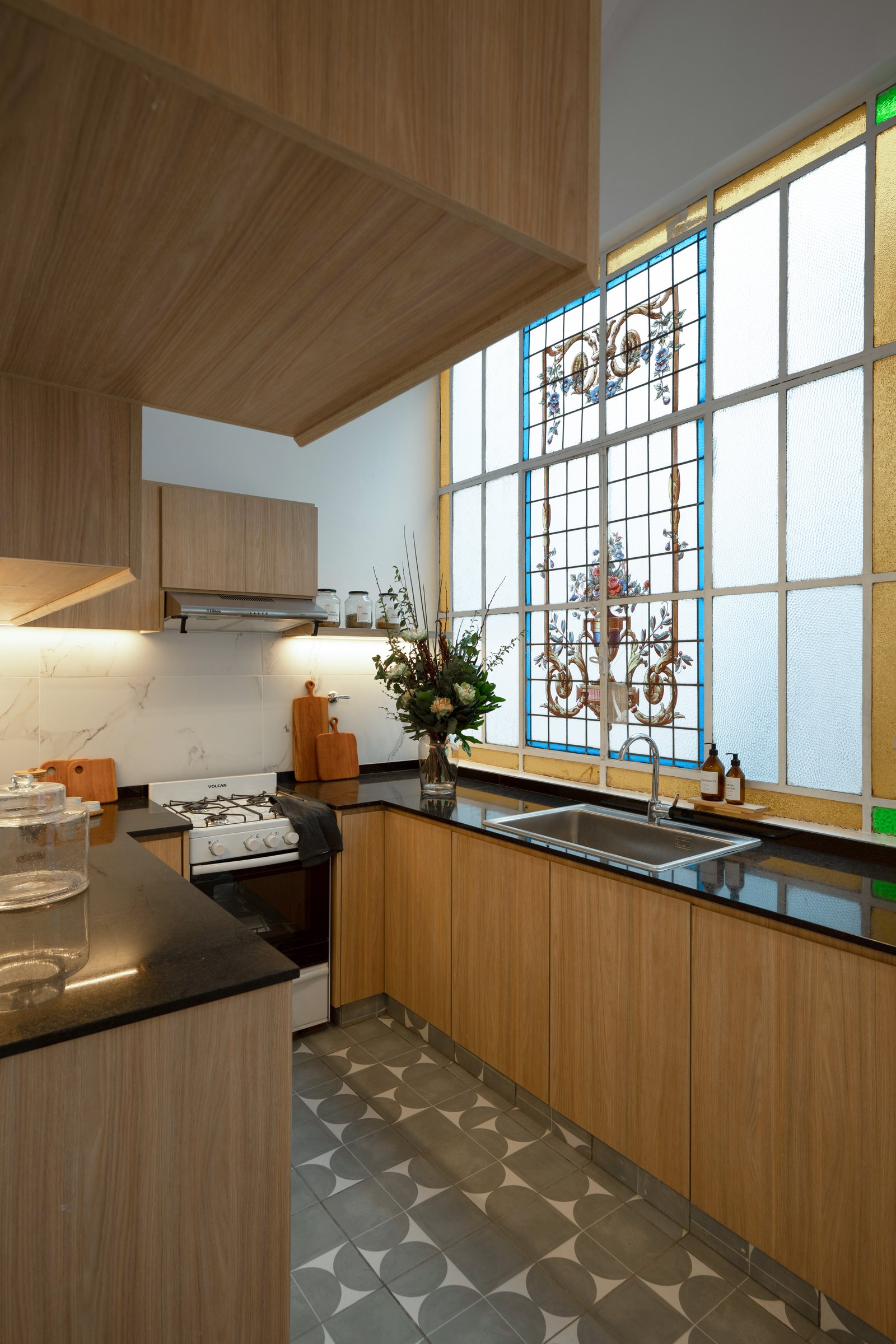 Cocina moderna con muebles de madera, mesada negra y vitral — proyecto Casa Gainza, por Estudio Plats, en Caballito